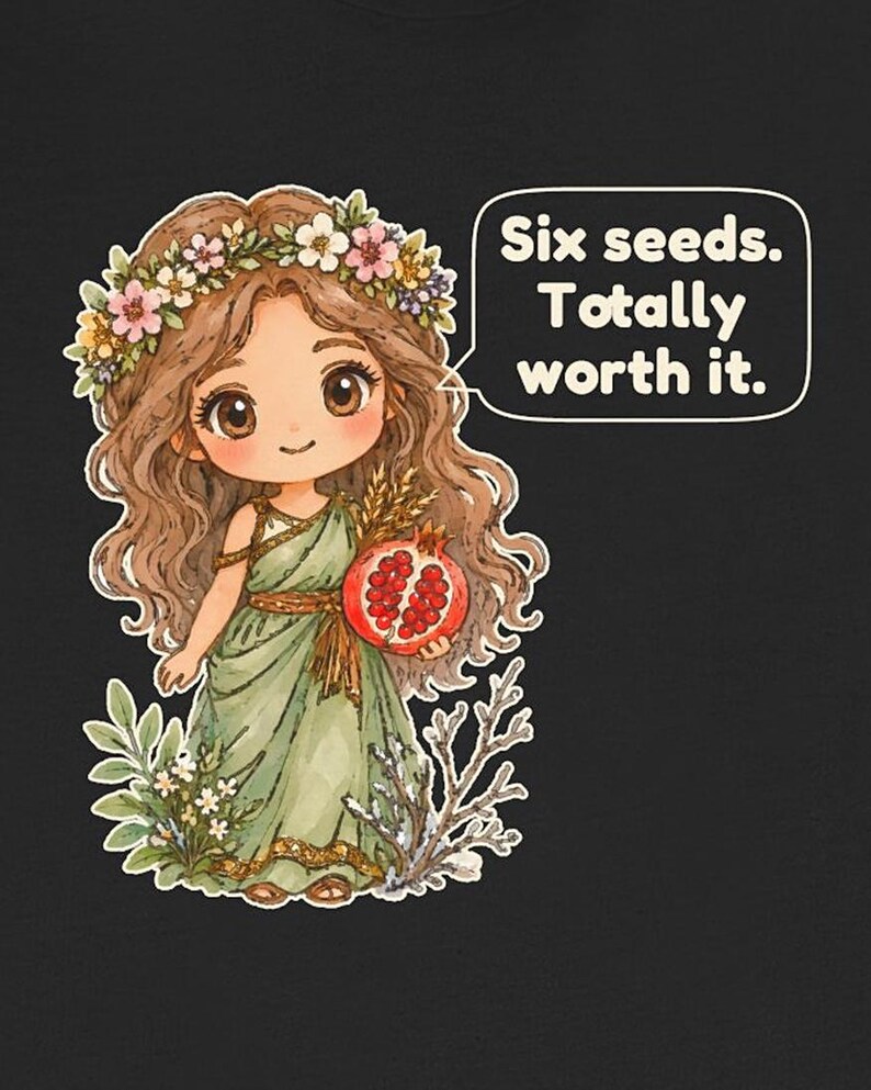 May include: A black t-shirt featuring a cartoon illustration of a girl with long brown hair wearing a flower crown and a green dress. She holds a pomegranate and wheat. A speech bubble contains the text: Six seeds. Totally worth it.