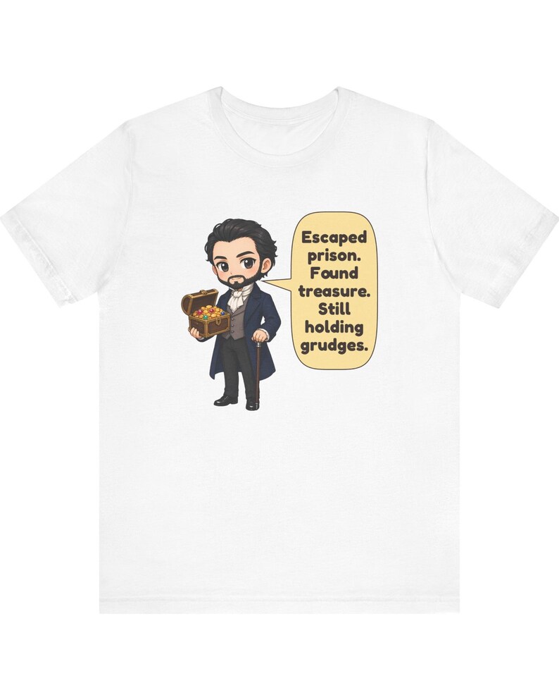 May include: A white t-shirt featuring a cartoon illustration of a bearded character in a dark blue coat holding a treasure chest. A speech bubble next to the character contains the text: Escaped prison. Found treasure. Still holding grudges.