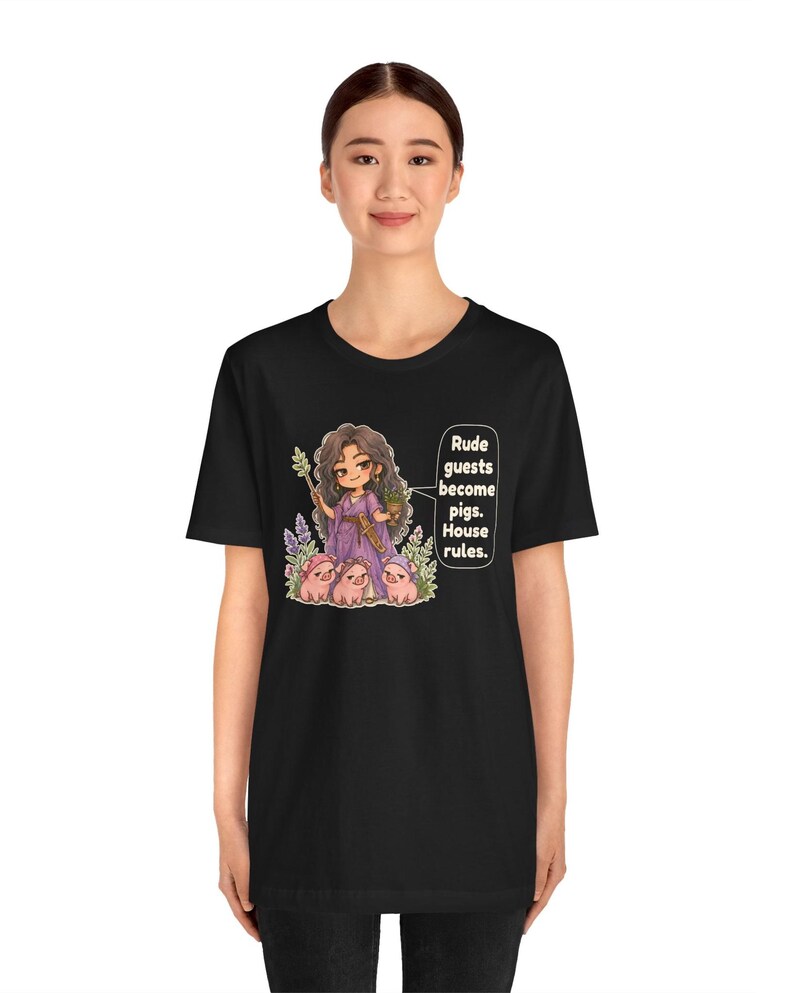 May include: A black t-shirt featuring a graphic of a character in a purple dress holding a wand and a potted plant, surrounded by three small pigs. A speech bubble contains the text: Rude guests become pigs. House rules.