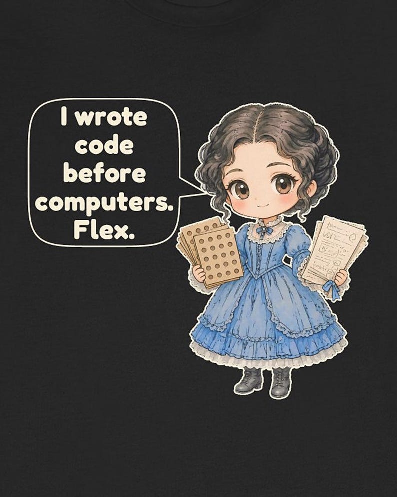 May include: A black t-shirt featuring a cartoon illustration of a person in a blue Victorian-style dress holding punch cards and papers. A speech bubble contains the text: I wrote code before computers. Flex.