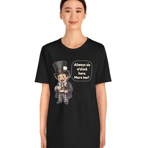 May include: A black short-sleeve t-shirt featuring a graphic of a character wearing a top hat and bowtie, holding a teacup and saucer. Next to the character is a speech bubble with the text: Always six o'clock here. More tea?