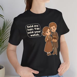 May include: A black t-shirt featuring a graphic of two cartoon characters in brown clothing. One character holds a small box, and a speech bubble contains the text: Sold my hair. You sold your watch. The design is centered on the chest area.