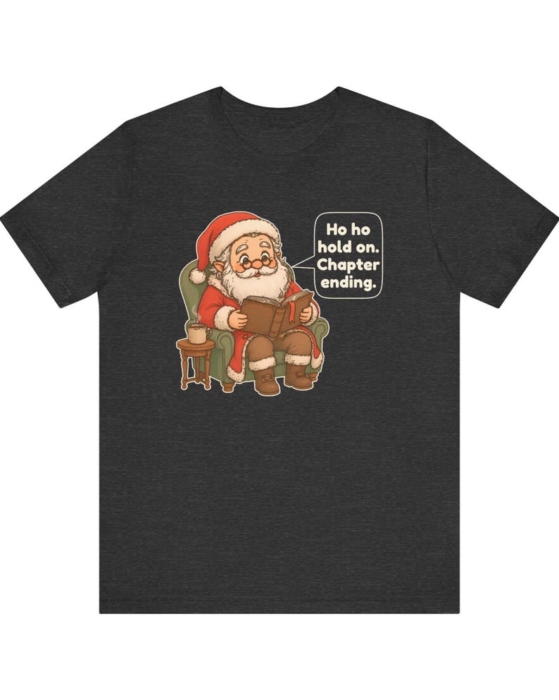 Op de afbeelding: Een donkergrijs gem&ecirc;leerd t-shirt met een afbeelding van de Kerstman die in een groene fauteuil zit en een boek leest, met een klein bijzettafeltje en een mok. Een tekstballon bevat de tekst: Ho ho hold on. Chapter ending.