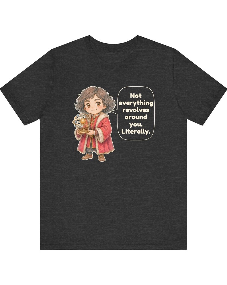 May include: A charcoal gray t-shirt featuring a cartoon illustration of a person with curly brown hair wearing a red coat, holding a golden armillary sphere. A speech bubble next to the figure contains the text: Not everything revolves around you. Literally.