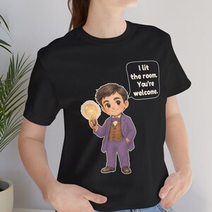 Może przedstawiać: Czarny t-shirt z rysunkową ilustracją osoby w fioletowym garniturze i brązowej kamizelce, trzymającej świecącą żar&oacute;wkę. Dymek z tekstem zawiera napis: I lit the room. You're welcome.