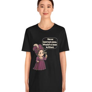 May include: A black t-shirt featuring a graphic of a person in a purple dress and hat holding a monocle. A speech bubble contains the text: Never learned piano. Would've been brilliant. The design is centered on the front of the garment.