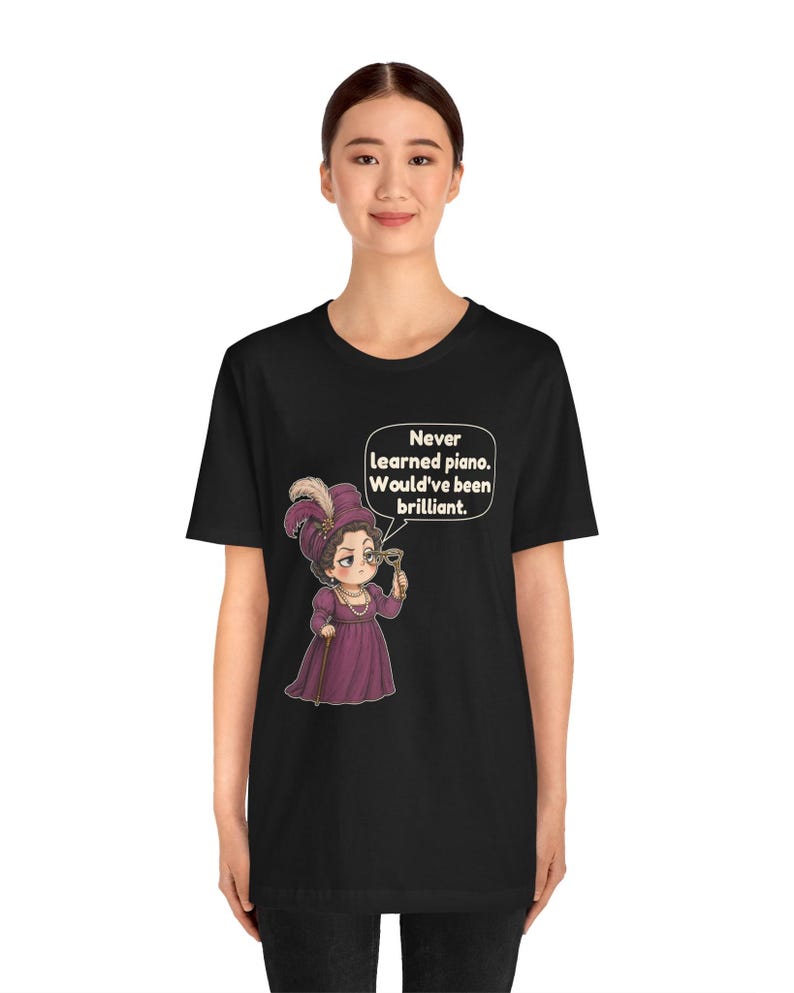 May include: A black t-shirt featuring a graphic of a person in a purple dress and hat holding a monocle. A speech bubble contains the text: Never learned piano. Would've been brilliant. The design is centered on the front of the garment.