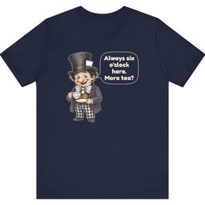 May include: A navy blue short-sleeve t-shirt featuring a graphic of a character in a top hat holding a teacup. A speech bubble next to the character contains the text: Always six o'clock here. More tea? The character wears a polka dot bow tie.