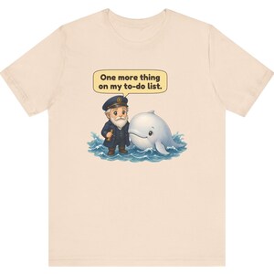 May include: A light beige t-shirt featuring a graphic of a bearded sea captain in a navy uniform standing next to a white whale in blue ocean waves. Above the characters, a speech bubble contains the text, One more thing on my to-do list.
