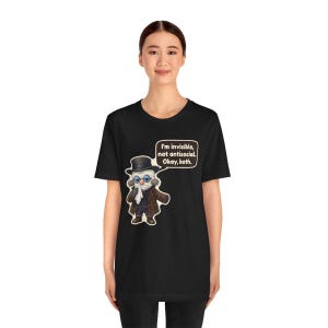 May include: A black t-shirt featuring a graphic of a bandaged figure wearing a top hat, glasses, and a brown coat. A speech bubble above the figure contains the text: I'm invisible, not antisocial. Okay, both.