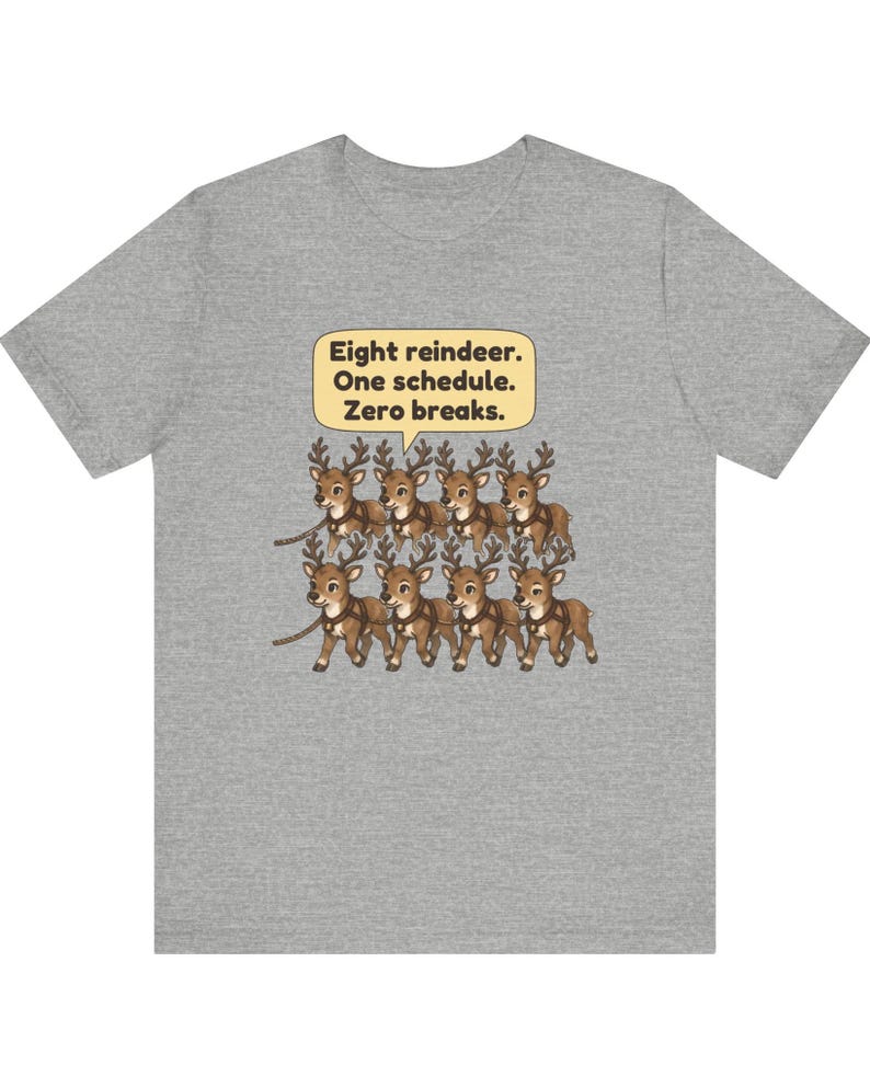 K&ouml;nnte beinhalten: Ein graues, meliertes T-Shirt mit einer Grafik von acht braunen Rentieren in zwei Reihen. &Uuml;ber den Rentieren befindet sich eine gelbe Sprechblase mit dem schwarzen Text: Eight reindeer. One schedule. Zero breaks.