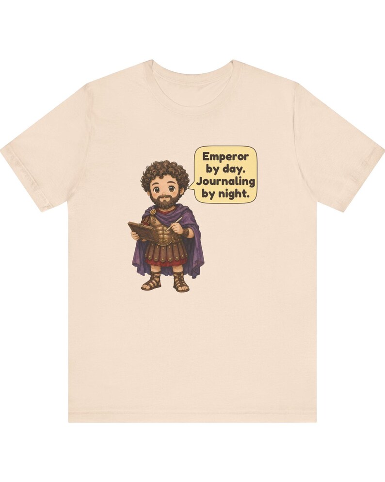 K&ouml;nnte beinhalten: Ein hellbeiges T-Shirt mit einer Cartoon-Illustration eines b&auml;rtigen Kaisers in r&ouml;mischer R&uuml;stung und violettem Umhang, der ein Tagebuch und einen Stift h&auml;lt. Eine Sprechblase neben der Figur enth&auml;lt den Text: Emperor by day. Journaling by night.