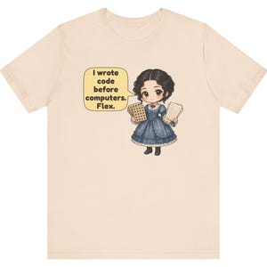 May include: A light beige t-shirt featuring a cartoon illustration of a person in a blue Victorian-style dress holding punch cards and papers. A yellow speech bubble contains the text: I wrote code before computers. Flex.