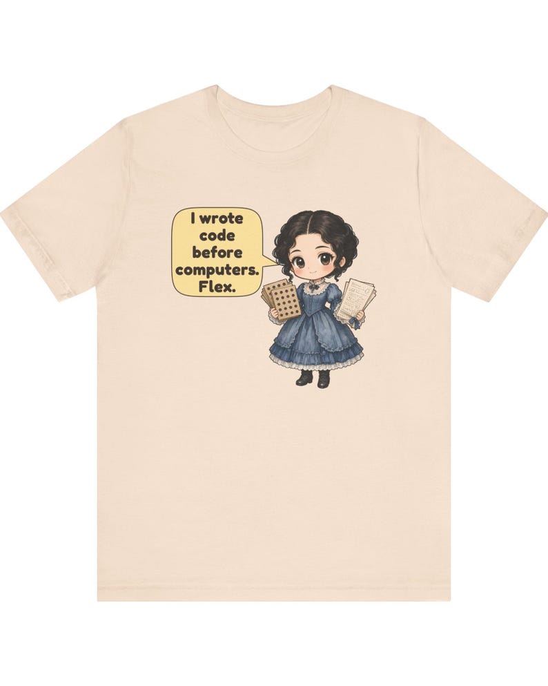 May include: A light beige t-shirt featuring a cartoon illustration of a person in a blue Victorian-style dress holding punch cards and papers. A yellow speech bubble contains the text: I wrote code before computers. Flex.