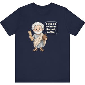 May include: A navy blue t-shirt featuring a cartoon illustration of a white-haired, bearded figure in a light gray toga holding a scroll and a brown pot, with a speech bubble containing the text: First, do no harm. Second, coffee.