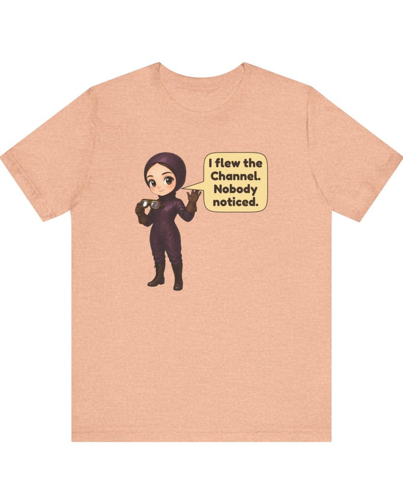 Puede incluir: Una camiseta color melocot&oacute;n con un personaje de dibujos animados con traje de vuelo morado y gafas. Un bocadillo junto al personaje contiene el texto: I flew the Channel. Nobody noticed. El dise&ntilde;o est&aacute; centrado en la parte delantera.