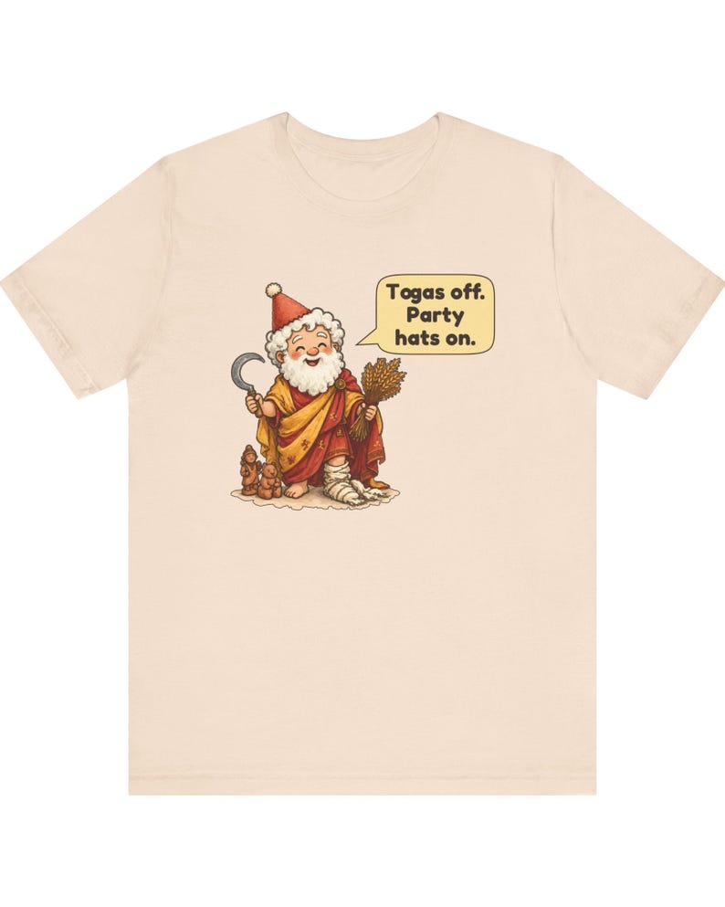 May include: A light beige t-shirt featuring a cartoon illustration of a bearded figure wearing a red and yellow robe, a red hat, and holding a sickle and wheat. A speech bubble contains the text: Togas off. Party hats on.