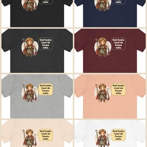 May include: A collection of eight t-shirts in various colours, each featuring a graphic of an angel holding a staff and a fish, with a speech bubble containing the text: God heals. I just do house calls.