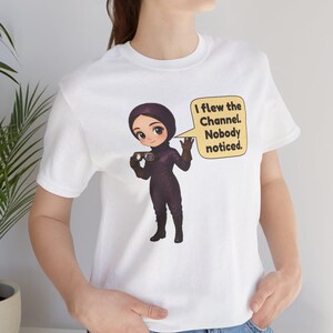 Puede incluir: Una camiseta blanca de manga corta con una ilustraci&oacute;n de dibujos animados de un piloto con traje de vuelo y casco de color morado oscuro, sosteniendo unas gafas. Un bocadillo amarillo contiene el texto: I flew the Channel. Nobody noticed.
