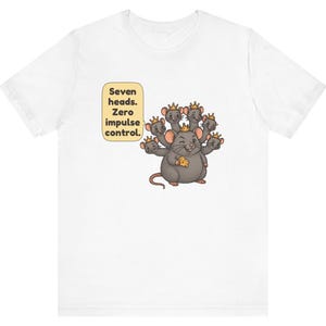 May include: A white t-shirt featuring a graphic of a gray rat with seven heads, each wearing a small gold crown. The rat holds a piece of yellow cheese. A speech bubble next to the rat contains the text: Seven heads. Zero impulse control.