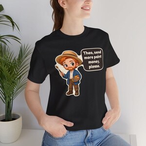 May include: A black t-shirt featuring a cartoon illustration of a red-haired artist wearing a straw hat, blue jacket, and brown pants. The artist holds a paintbrush and palette. A speech bubble contains the text: Theo, send more paint money, please.