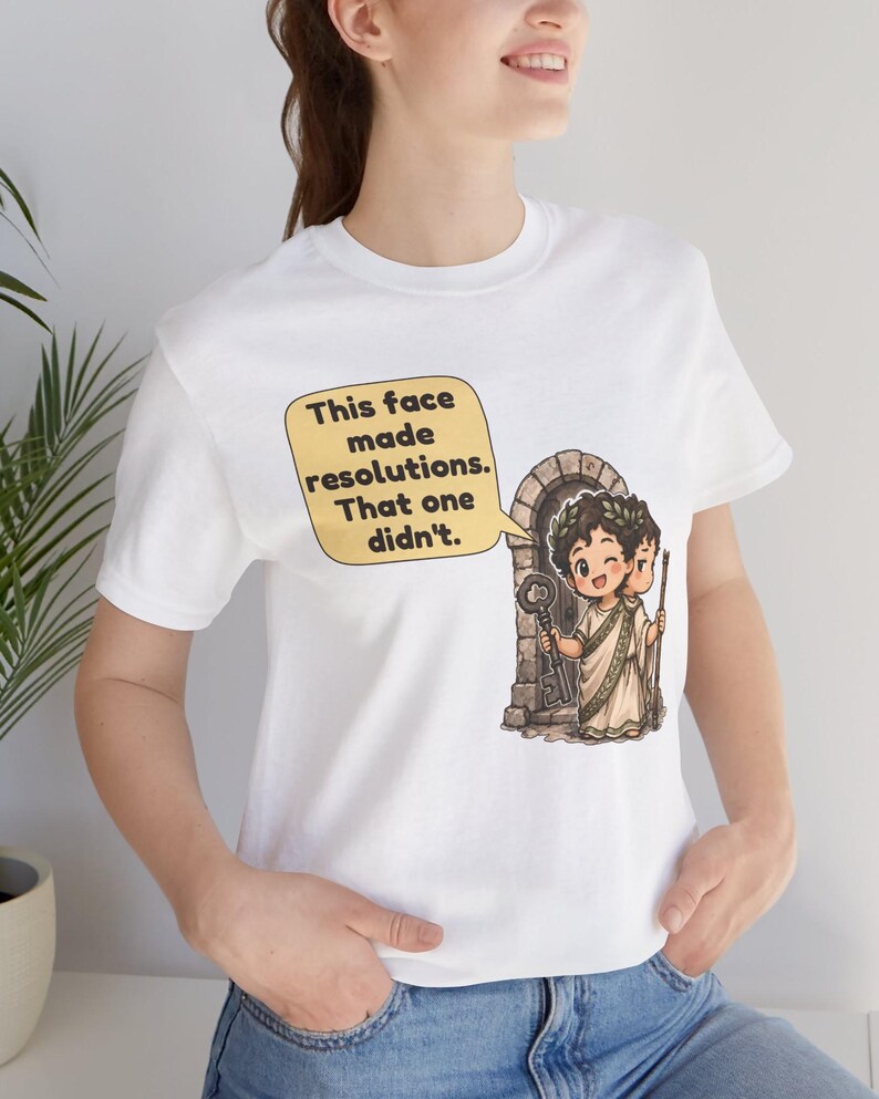 K&ouml;nnte beinhalten: Ein wei&szlig;es T-Shirt mit einer Grafik einer zweigesichtigen Cartoon-Figur in einer Toga vor einem Steintor. Eine Sprechblase enth&auml;lt den Text: This face made resolutions. That one didn't. Die Figur h&auml;lt einen gro&szlig;en Schl&uuml;ssel und einen Stab.