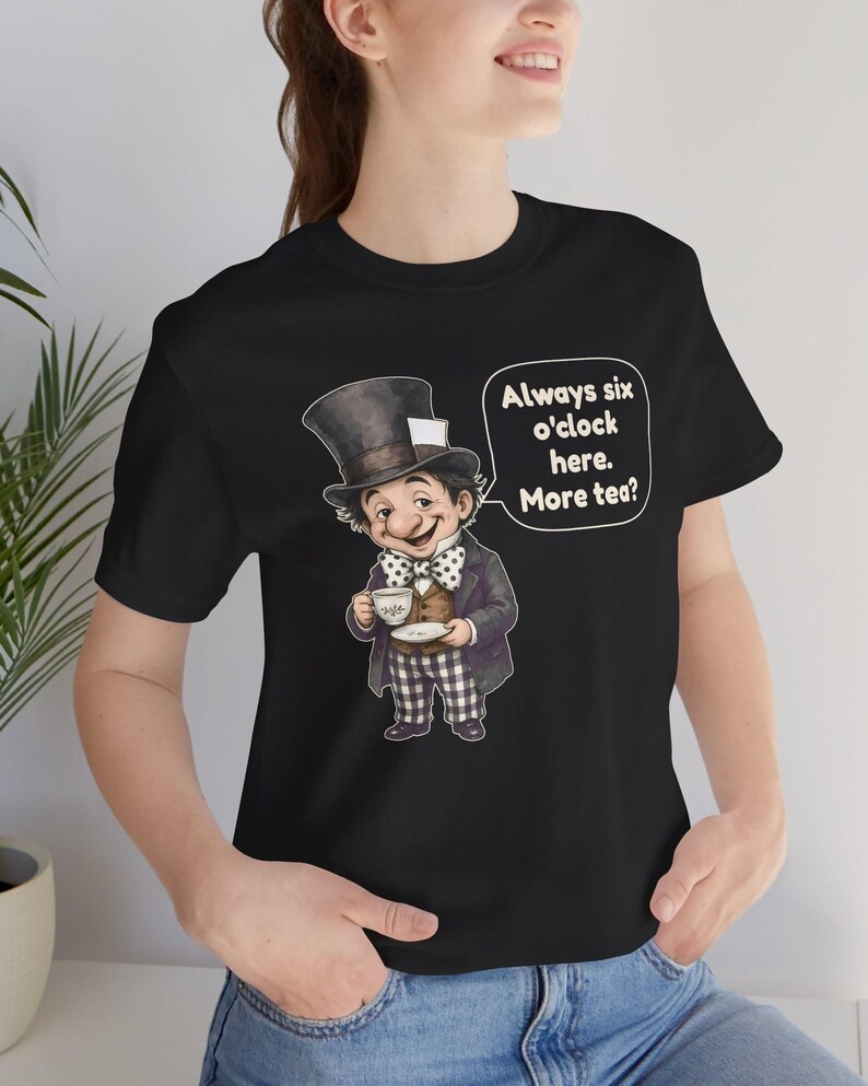 May include: A black t-shirt featuring a graphic of a character wearing a top hat, a polka dot bow tie, a brown vest, and checkered pants, holding a teacup. A speech bubble next to the character contains the text: Always six o'clock here. More tea?