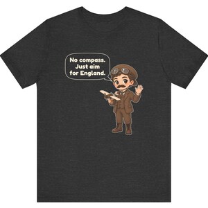 May include: A dark heather gray t-shirt featuring a cartoon illustration of a pilot with a mustache, goggles, and a brown suit holding a small airplane. A speech bubble contains the text: No compass. Just aim for England.