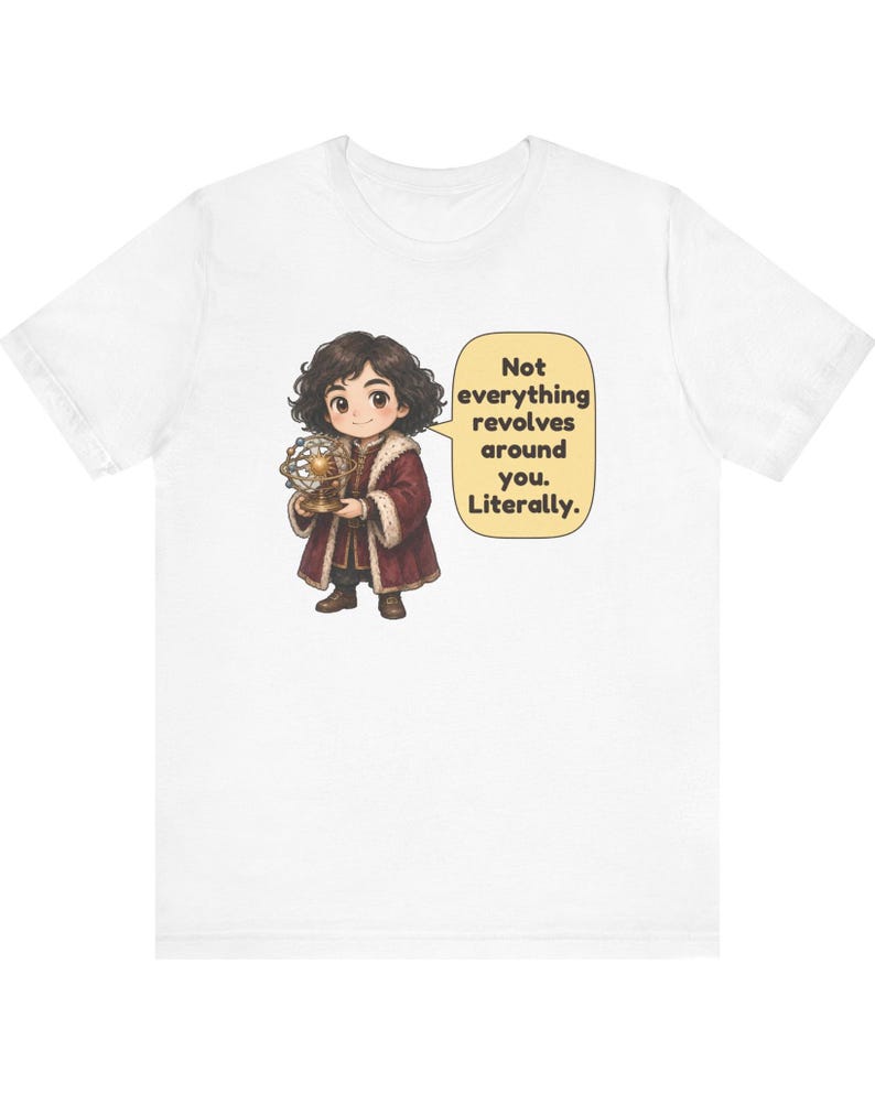 May include: A white t-shirt featuring a cartoon illustration of a person with dark curly hair wearing a maroon coat with fur trim, holding a gold model of a solar system. A speech bubble contains the text: Not everything revolves around you. Literally.