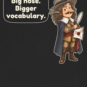 May include: A black t-shirt featuring a cartoon illustration of a person with long brown hair, a mustache, and a large nose, wearing a wide-brimmed hat with a feather, a cape, and boots, holding a quill and letter. Text reads: Big nose. Bigger vocabulary.