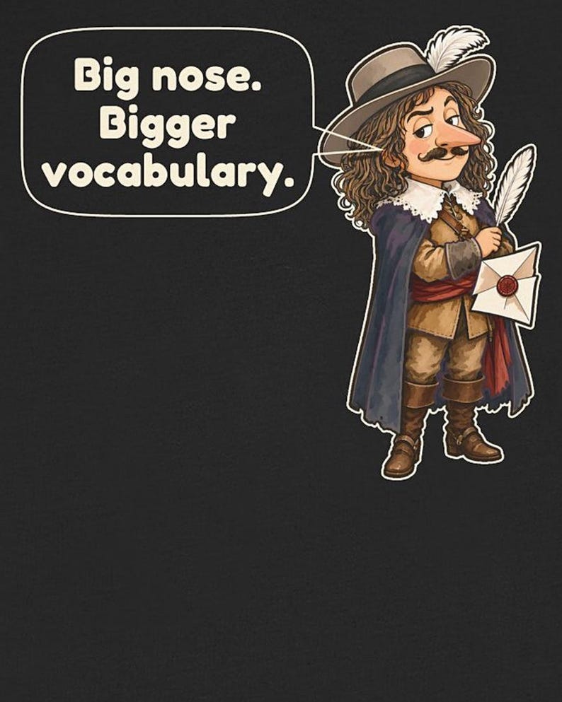 May include: A black t-shirt featuring a cartoon illustration of a person with long brown hair, a mustache, and a large nose, wearing a wide-brimmed hat with a feather, a cape, and boots, holding a quill and letter. Text reads: Big nose. Bigger vocabulary.