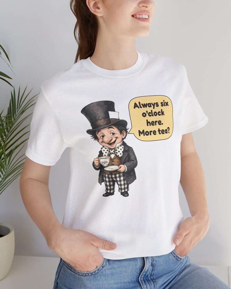 May include: A white t-shirt featuring a graphic of a character wearing a top hat, a polka dot bow tie, a dark jacket, and checkered pants, holding a teacup. A yellow speech bubble contains the text: Always six o'clock here. More tea?