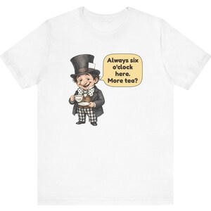 May include: A white t-shirt featuring a graphic of a character wearing a tall top hat, a brown vest, and black and white checkered pants. The character holds a teacup and saucer. A speech bubble contains the text: Always six o'clock here. More tea?