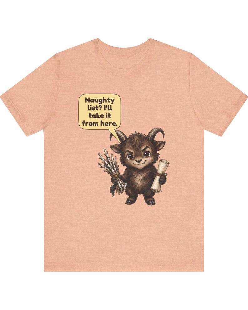 Puede incluir: Una camiseta de color melocot&oacute;n con un gr&aacute;fico de una peque&ntilde;a criatura marr&oacute;n oscuro con cuernos que sostiene un manojo de palos y un pergamino. Un bocadillo amarillo sobre la criatura contiene el texto: Naughty list? I'll take it from here.