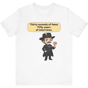 Pu&ograve; includere: Una t-shirt bianca con un'illustrazione a cartoni animati di un uomo con i baffi che indossa un cappello e un cappotto neri, mentre tiene in mano delle carte da gioco. Un fumetto contiene il testo: Thirty seconds of fame. Fifty years of interviews.