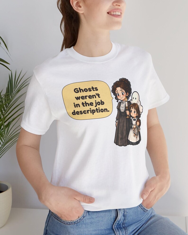 Op de afbeelding: Een wit t-shirt met korte mouwen en een afbeelding van een vrouw en een kind met een kaars, vergezeld door een klein spookje. Een gele tekstballon bevat de zwarte tekst: Ghosts weren't in the job description.