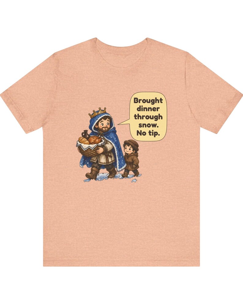 May include: A peach-colored t-shirt featuring a cartoon illustration of a person wearing a crown and blue cloak carrying a basket of food, accompanied by a child. A speech bubble contains the text: Brought dinner through snow. No tip.