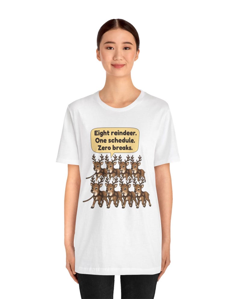 K&ouml;nnte beinhalten: Ein wei&szlig;es Kurzarm-T-Shirt mit einer Grafik von acht braunen Rentieren in zwei Reihen. &Uuml;ber den Rentieren befindet sich eine gelbe Sprechblase mit dem Text: Eight reindeer. One schedule. Zero breaks.