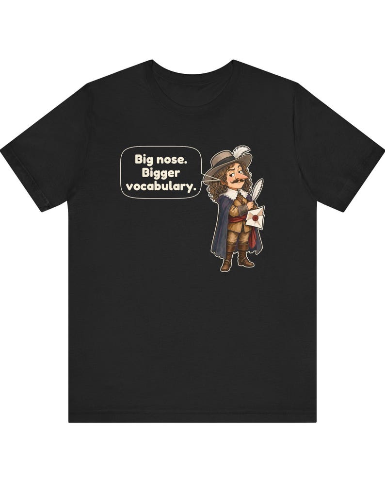 May include: A black short-sleeved t-shirt featuring a cartoon illustration of a historical figure with a large nose, wearing a hat and cape, holding a quill and letter. A speech bubble contains the text: Big nose. Bigger vocabulary.