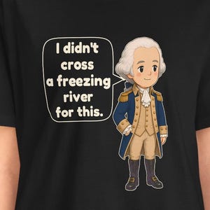 May include: A black t-shirt featuring a cartoon illustration of a historical figure in a blue coat, tan vest, and white cravat. A speech bubble next to the figure contains the text: I didn't cross a freezing river for this.