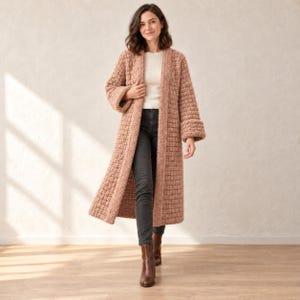 May include: A long, dusty rose-colored open-front cardigan featuring a chunky, textured knit pattern with wide sleeves and folded cuffs, worn over a white top and dark gray jeans with brown leather ankle boots.