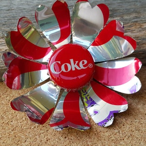Puede incluir: Una flor roja y plateada hecha de una lata de Coca-Cola con una tapa de botella roja de Coca-Cola en el centro.