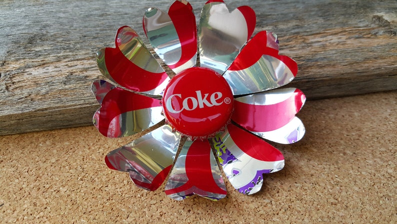 Puede incluir: Una flor roja y plateada hecha de una lata de Coca-Cola con una tapa de botella roja de Coca-Cola en el centro.