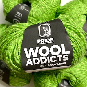 Puede incluir: Madejas de hilo verde con una etiqueta negra que dice "PRIDE WOOL ADDICTS BY LANGYARNS".