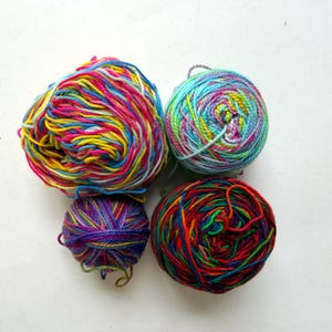 May include: Four colorful yarn skeins in various sizes. The yarn is a mix of bright colors including pink, yellow, blue, and green. The yarn is tightly wound into balls, perfect for knitting or crocheting projects.