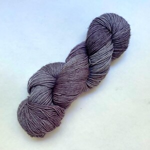May include: A skein of yarn in shades of gray and purple, with a twisted, rope-like appearance. The yarn appears soft and is likely made of natural fibers. Ideal for knitting or crocheting projects.
