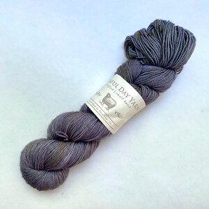 May include: A skein of gray yarn with subtle color variations and a label that reads "Joyful Day Yarn." The yarn is a soft, textured material, ideal for knitting or crocheting projects. The label features a sheep illustration.