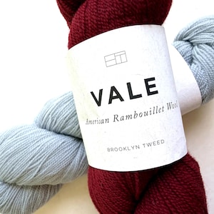May include: Two skeins of yarn, one deep burgundy and one light blue, wrapped in a white paper label. The label features the text VALE, American Rambouillet Wool, and BROOKLYN TWEED, along with a small geometric logo at the top center.