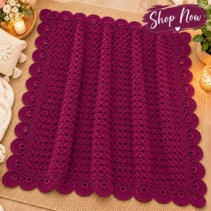 May include: A rectangular magenta crochet blanket featuring a textured, repeating stitch pattern throughout the center and a decorative scalloped border with circular cutouts along all four edges. The blanket is a deep, solid shade of pink.
