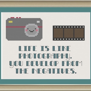 Puede incluir: Un diseño de punto de cruz con una cámara de dibujos animados y una tira de película. El texto dice "La vida es como la fotografía. Te desarrollas a partir de los negativos."